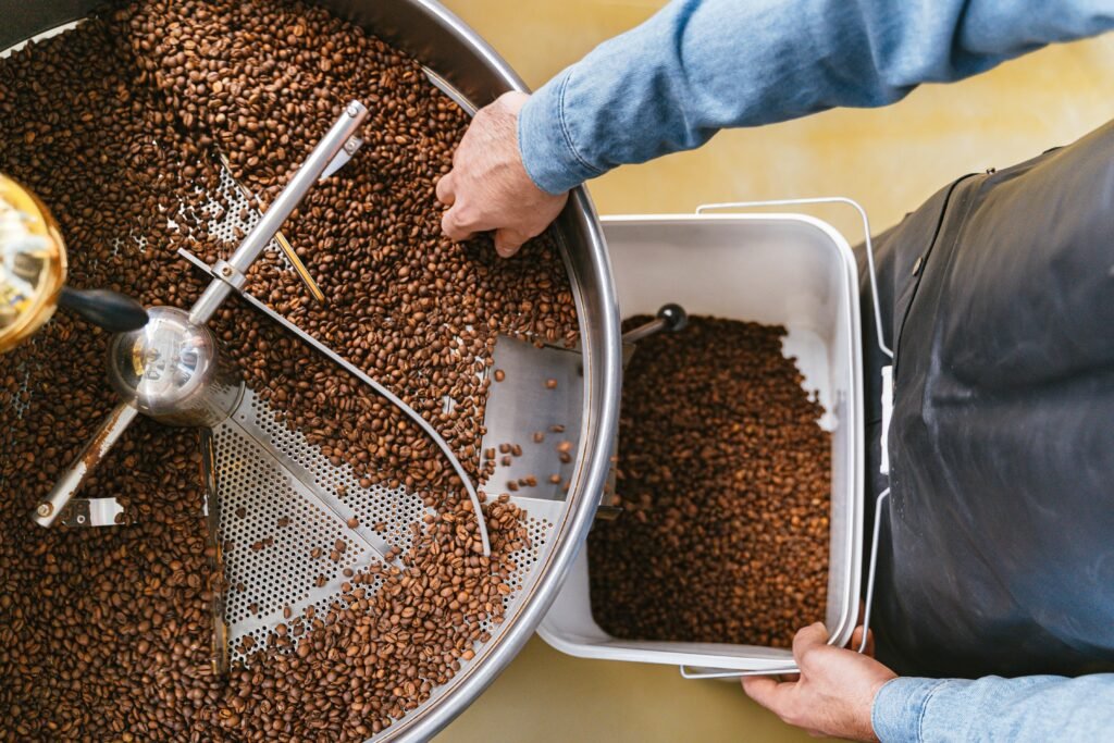 Hands delicately managing freshly roasted coffee beans in a roaster from a top view.